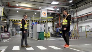 Két munkatárs találkozik a raktárban, miközben a Linde Secure Distance Vestet és a Linde Distance Beepert viselik.