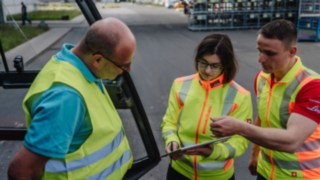 Három, biztonsági mellényt viselő ember beszélget: biztonsági tanácsadás az ügyfél telephelyén. Három, biztonsági mellényt viselő ember beszélget: biztonsági tanácsadás az ügyfél telephelyén.