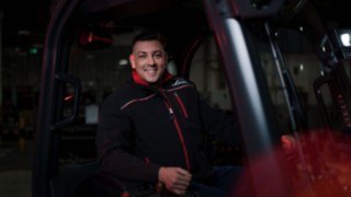 A Linde egy alkalmazottja egy anyagmozgató gépben ül, és a kamerába mosolyog.