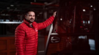 A Linde egy alkalmazottja egy anyagmozgató gép mellett áll, és a kamerába mosolyog.